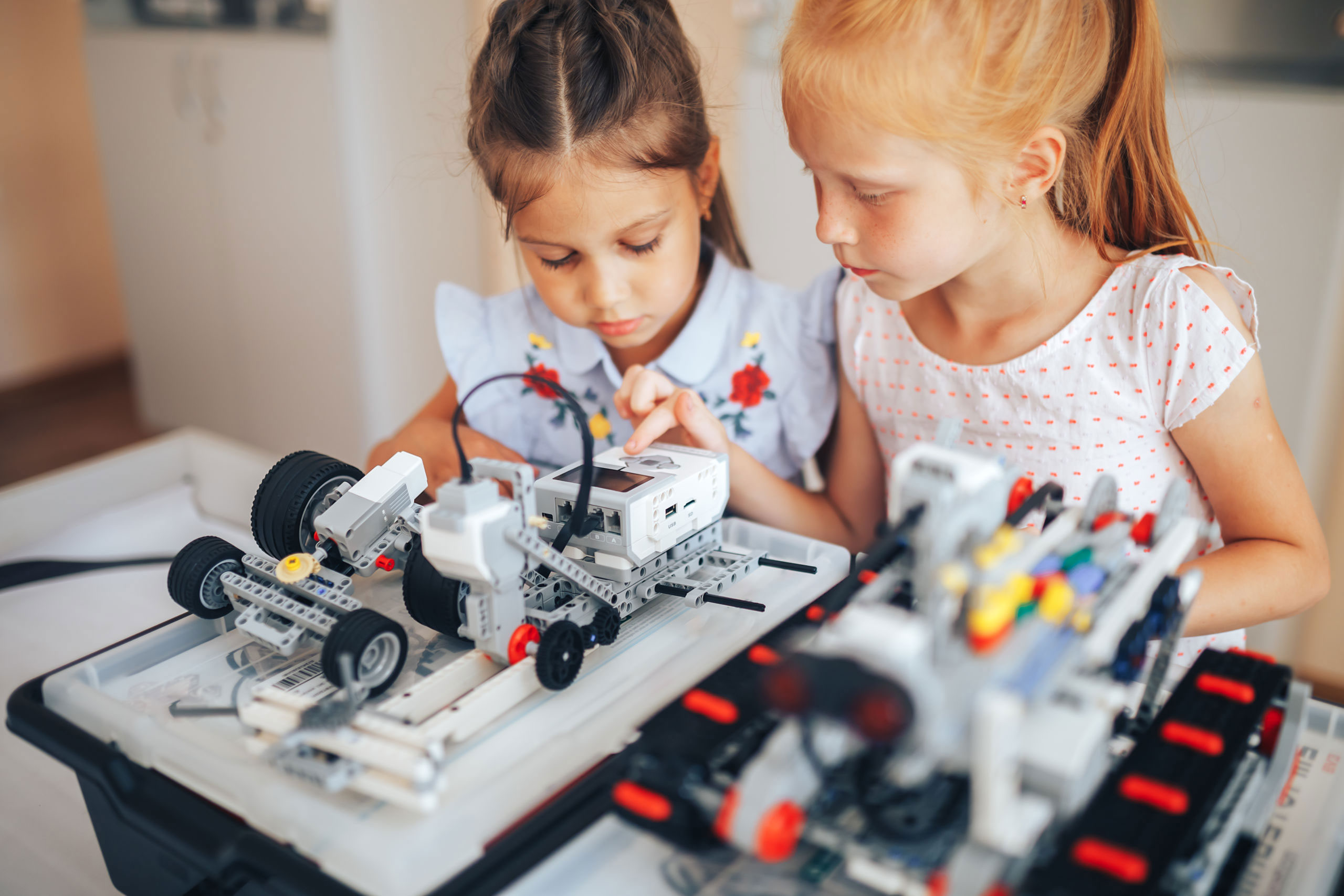 Two schoolgirls study in a robotics class, assemble a robot constructor